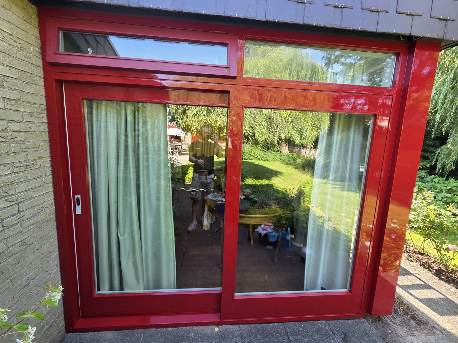 Rood gelakte schuifpui en kozijn van een aanbouw aan de tuinkant
